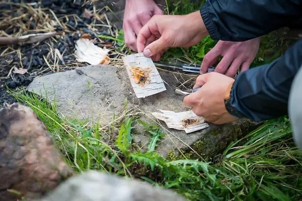 Zunder glimmt auf einem Stein, während zwei Hände mit Werkzeugen arbeiten