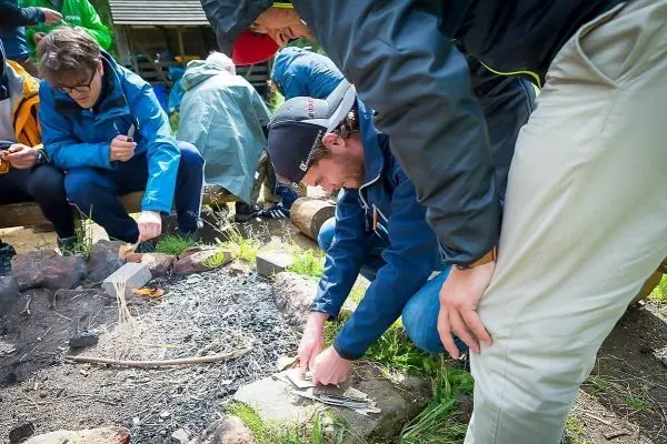 Zunder wird am Bodenfeuer vorbereitet, während Teilnehmer um das Feuer versammelt sind