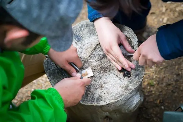 Zwei Hände bearbeiten einen Holzblock mit einem Messer und Zunder