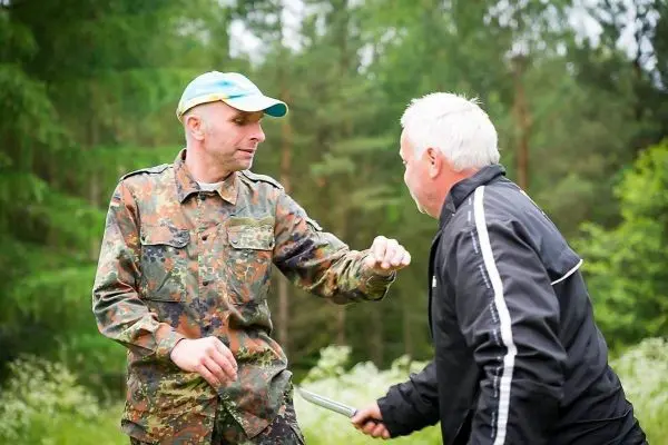 Zwei Männer in Waldumgebung üben eine Selbstverteidigungstechnik mit einem Messer