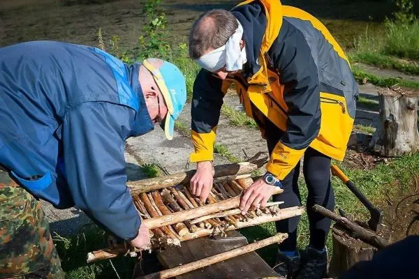 Zwei Personen bauen eine Holzstruktur aus Ästen auf einem Tisch