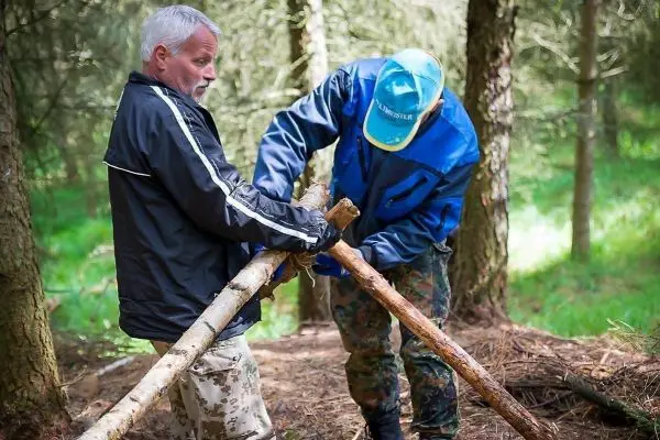 Zwei Personen bauen eine selbstgebaute Konstruktion aus Holzstöcken im Wald