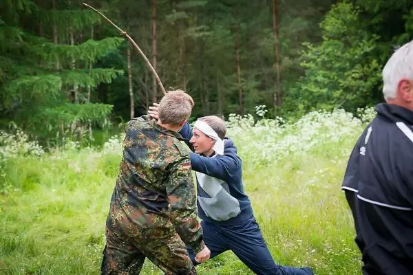 Zwei Personen im Nahkampf, einer mit einem Stock, im grünen Gelände