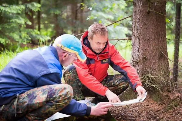 Zwei Personen studieren eine Karte im Wald neben einem Baum