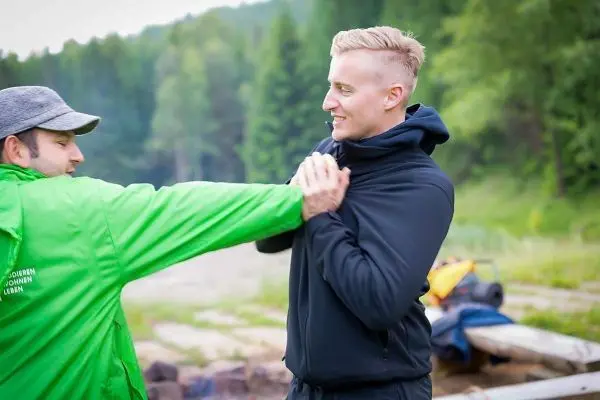 Zwei Personen üben eine körperliche Technik im Freien, eine Person greift die andere an