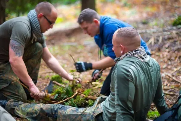 Drei Personen arbeiten am Boden mit Pflanzenmaterial und Ästen im Wald