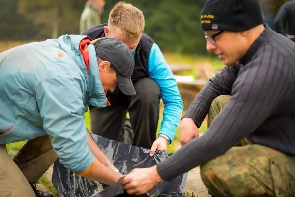 Drei Personen arbeiten gemeinsam an einer schwarzen Plane auf dem Boden