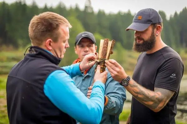Drei Personen binden Holzstücke mit Schnur zu einer Konstruktion zusammen