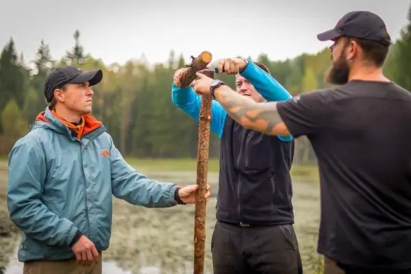 Drei Personen halten einen langen Stock, während sie ihn zusammen bearbeiten
