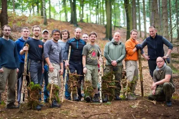 Gruppe von Personen steht im Wald mit Stöcken in der Hand beim Überlebenstraining
