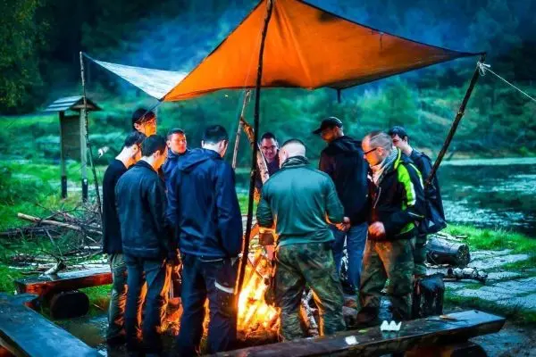 Gruppe von Personen steht um ein Feuer unter einem Zelt