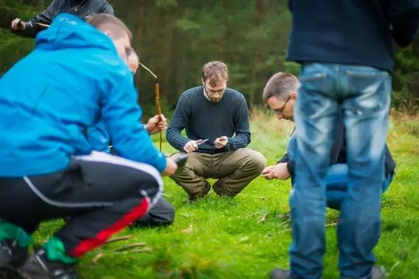 Gruppe von Personen übt das Schnitzen auf einer Wiese beim Survival Training