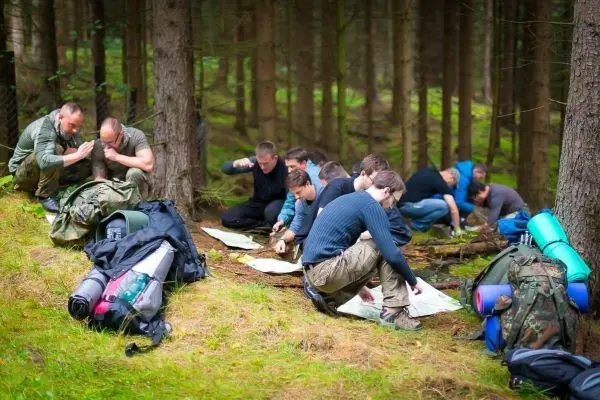 Gruppenmitglieder analysieren Karten im Wald, Rucksäcke und Matten liegen daneben