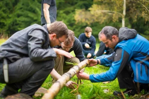 Gruppierung von Personen konstruiert selbstgebaute Seilbrücke aus einem Holzstamm