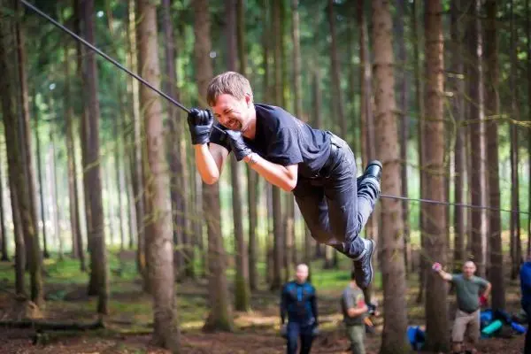Junge überquert selbstgebaute Seilbrücke zwischen Bäumen im Wald