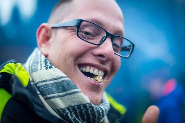 Lächelnder Mann mit Brille und Schal, Insekt im Mund