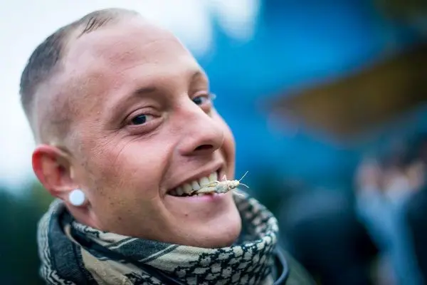 Lächelnder Mann mit einem Insekt im Mund und Schal um den Hals