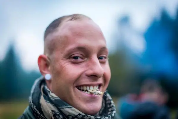 Lächelnder Mann mit einem Stück Zunder im Mund, im Hintergrund Rauch