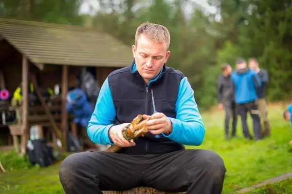 Mann bearbeitet Holzstück mit einem Messer auf einem Baumstumpf