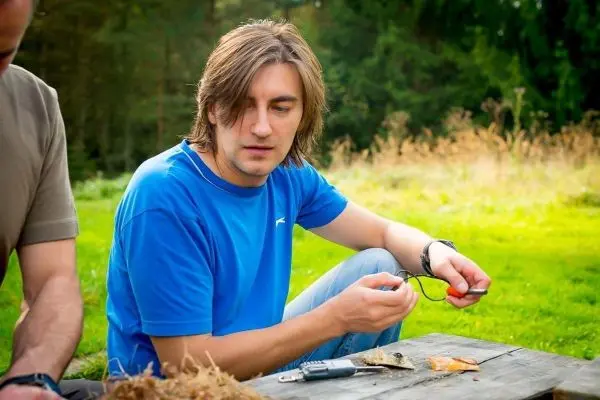 Mann hält Zunder in der Hand und schaut auf eine Holzoberfläche
