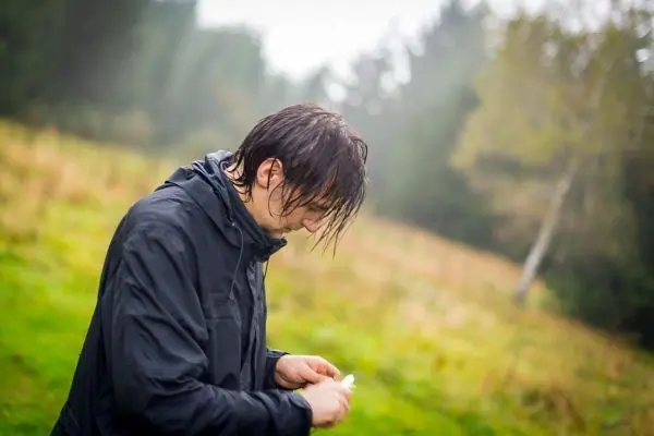 Mann in Regenjacke bearbeitet ein kleines Objekt im Freien