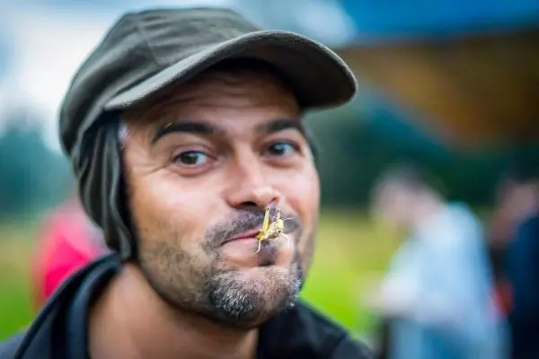 Mann mit einer Heuschrecke auf der Oberlippe und lächelndem Gesicht