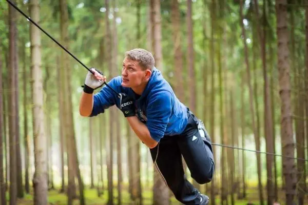Mann überquert eine selbstgebaute Seilbrücke zwischen Bäumen