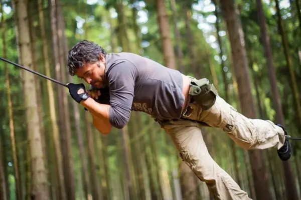 Mann überquert eine selbstgebaute Seilbrücke zwischen Bäumen