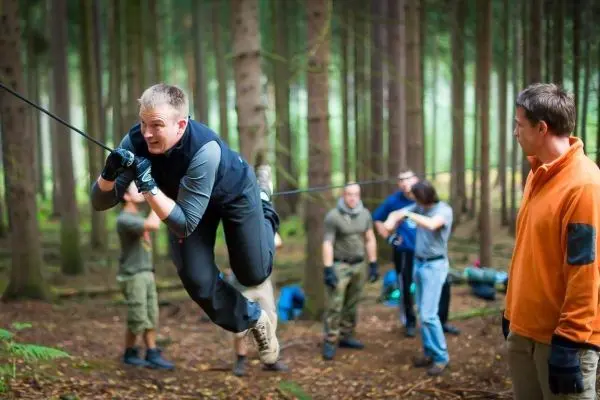 Mann überquert selbstgebaute Seilbrücke im Wald, während andere zuschauen