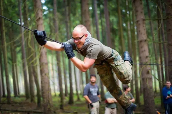 Mann überquert selbstgebaute Seilbrücke zwischen Bäumen im Wald