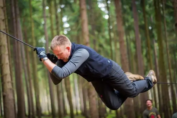 Mann überquert selbstgebaute Seilbrücke zwischen Bäumen im Wald