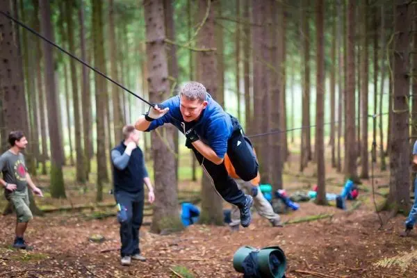 Mann überquert selbstgebaute Seilbrücke zwischen Bäumen im Wald