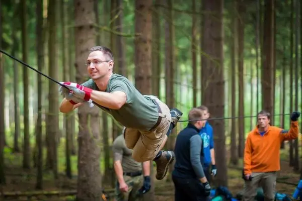 Mann überquert selbstgebaute Seilbrücke zwischen Bäumen im Wald