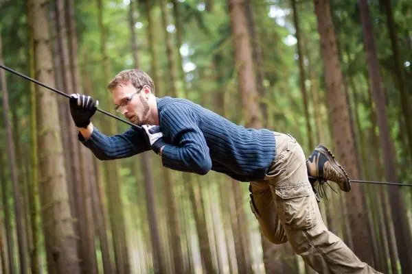 Mann überquert selbstgebaute Seilbrücke zwischen Bäumen im Wald