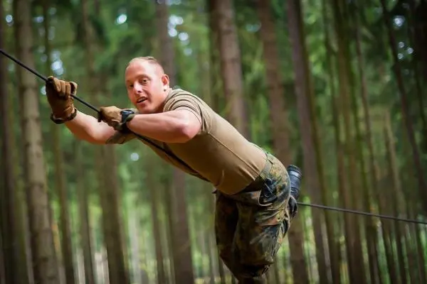Mann überquert selbstgebaute Seilbrücke zwischen Bäumen im Wald