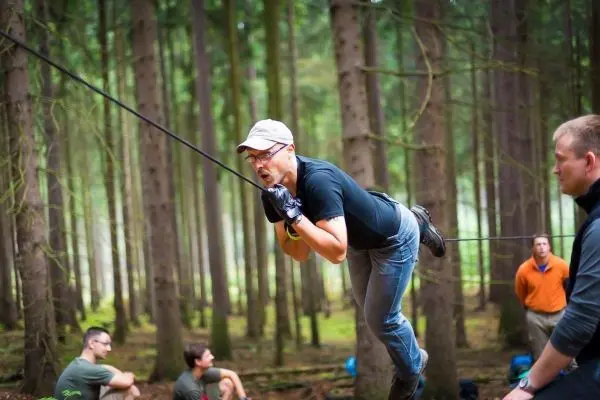 Mann überquert selbstgebaute Seilbrücke zwischen Bäumen im Wald