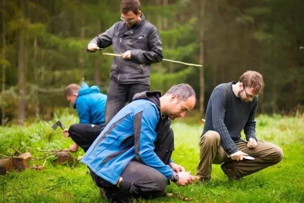 Mehrere Personen bearbeiten Holzstücke mit Messern und Werkzeugen im Wald