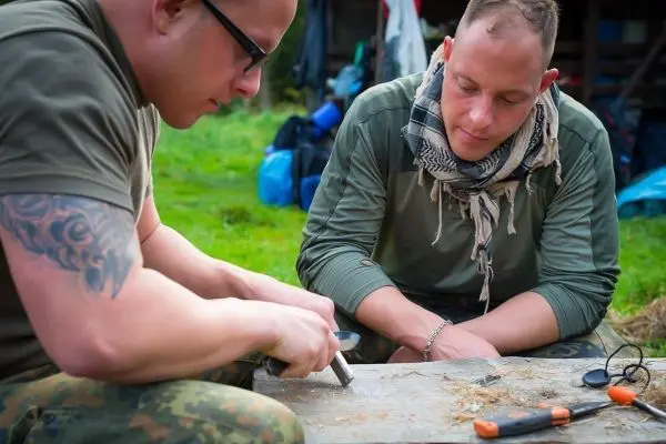 Messer bearbeitet Zunder auf einem Tisch, während zwei Personen konzentriert zuschauen