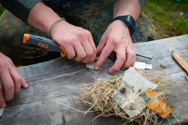 Messer schneidet Zunder aus Gras und Papier auf einem Holzbrett