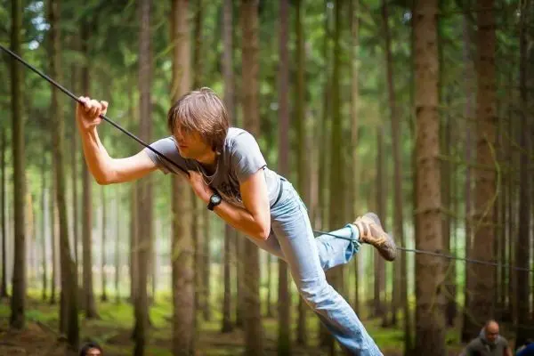 Person balanciert auf einer selbstgebauten Seilbrücke im Wald