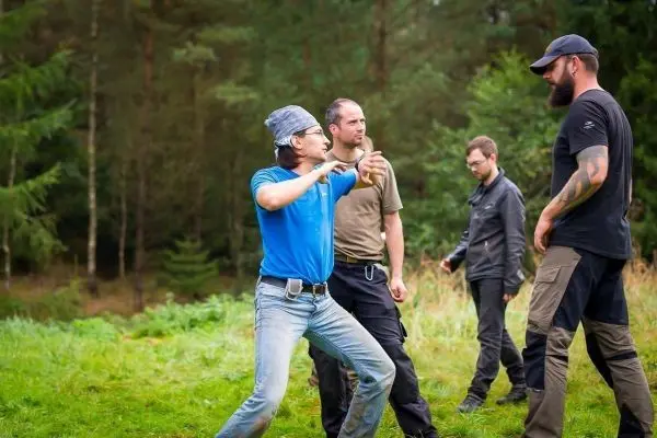 Person demonstriert eine Technik in einer Waldumgebung, während drei weitere Personen beobachten