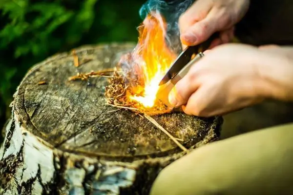 Person entzündet Feuer mit einem Feuerzeug auf einem Holzstamm beim Survival Training