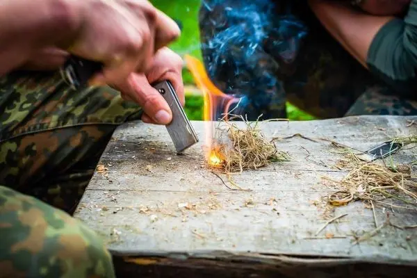 Person entzündet trockenes Gras mit einem Feuerstahl beim Überlebenstraining
