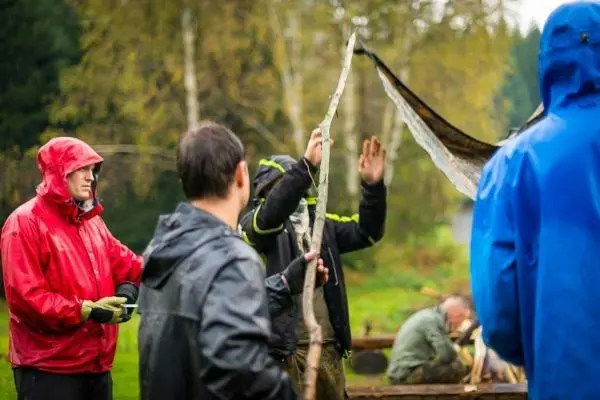Teilnehmer bauen eine Tarp-Notunterkunft mit einem Holzstock und einer Plane