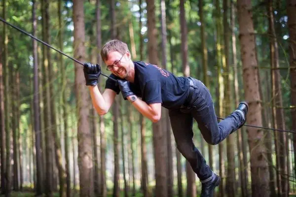 Überquert eine selbstgebaute Seilbrücke zwischen Bäumen im Wald