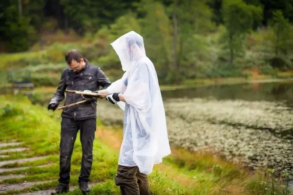 Zwei Personen am Ufer eines Gewässers, eine Person hält einen Stock