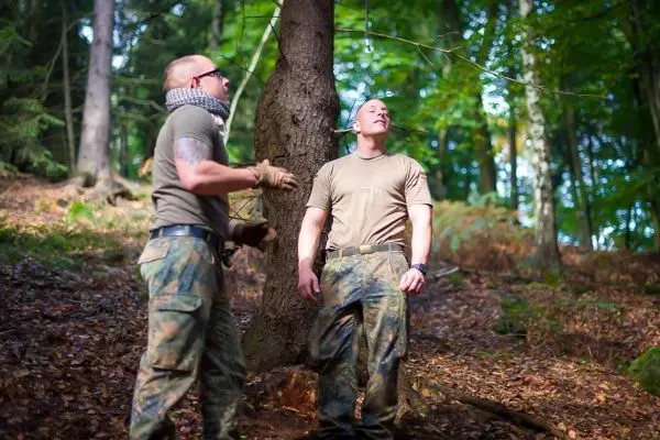 Zwei Personen arbeiten an einer selbstgebauten Seilbrücke zwischen Bäumen
