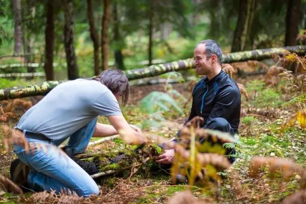 Zwei Personen arbeiten im Wald am Boden, eine Person gräbt mit den Händen