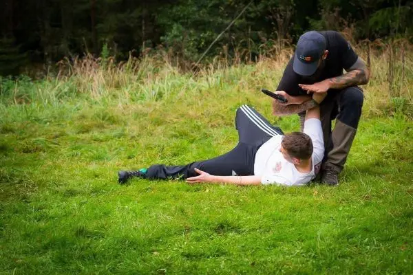 Zwei Personen auf Gras, eine Person hält die andere in einer kontrollierten Position