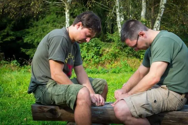 Zwei Personen bearbeiten Holz auf einem Baumstamm im Freien